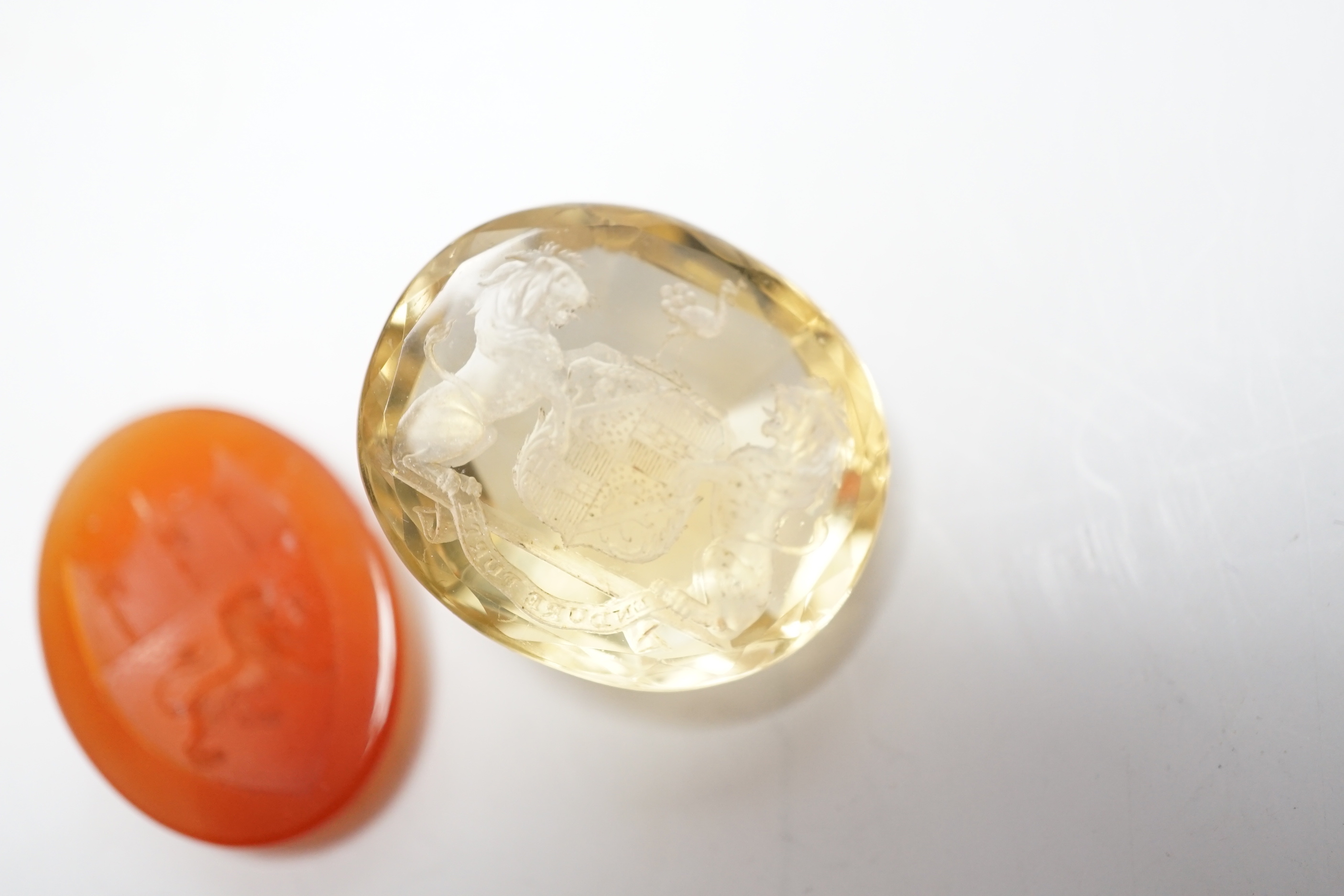 An unmounted oval cut intaglio citrine, 28mm by 25mm and a similar carnelian intaglio, both matrix carved with armorial/crest.